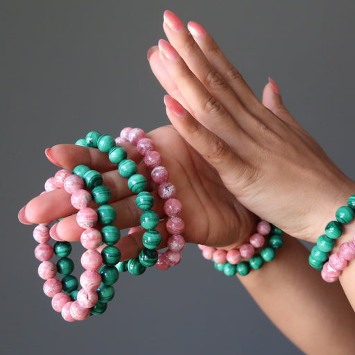 hand holding and wearing pink rhodochrosite and green malachite stretch bracelets