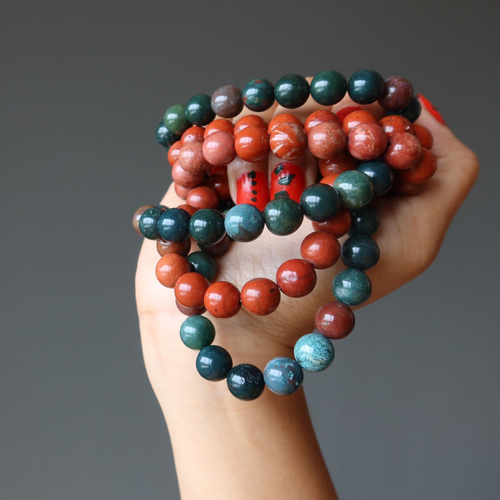 hand holding 3 sets of showing Red Jasper and Green Bloodstone beaded stretch bracelets 