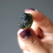 hand holding green moldavite gemstone with a scroll curl