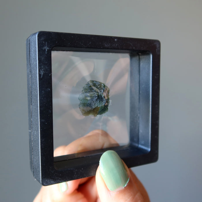 rough green moldavite gemstone in display case