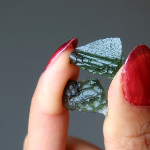 hand holding pair of moldavite rough gemstones