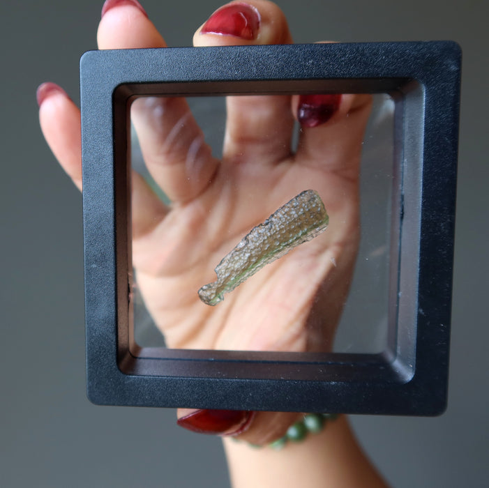 hand holding genuine moldavite gemstone in display case