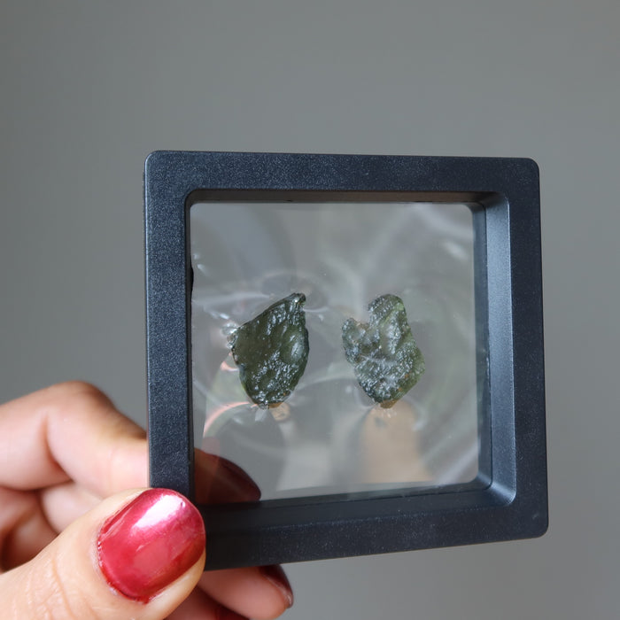 hand holding moldavite pair in a display case