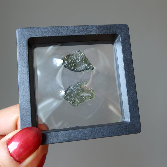 hand holding moldavite pair in a display case