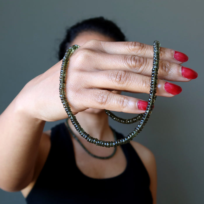 female wearing and holding moldavite faceted necklace