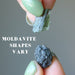 hands holding two pieces of moldavite to show that shapes vary
