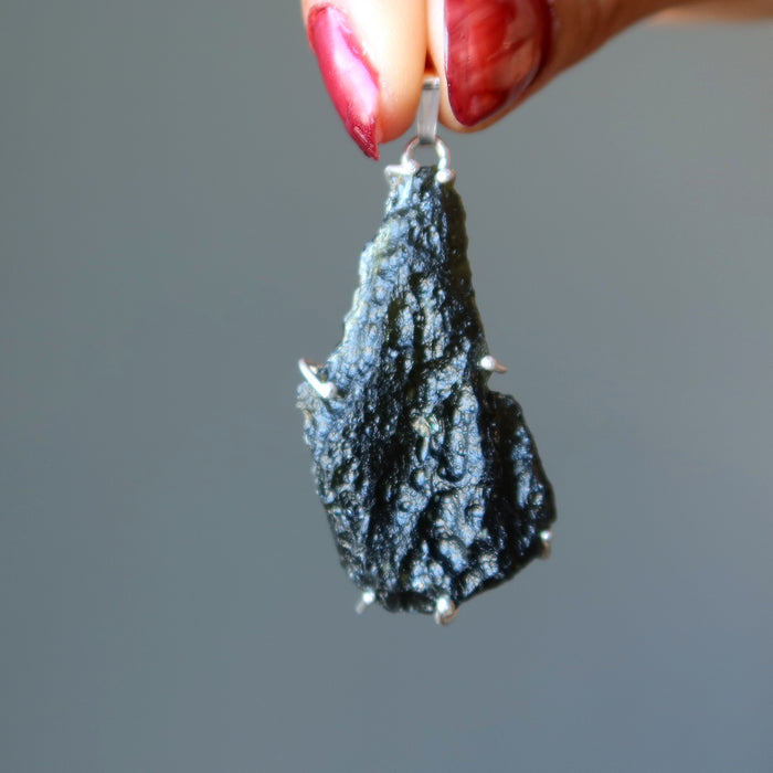 hand holding large raw moldavite in sterling silver pendant