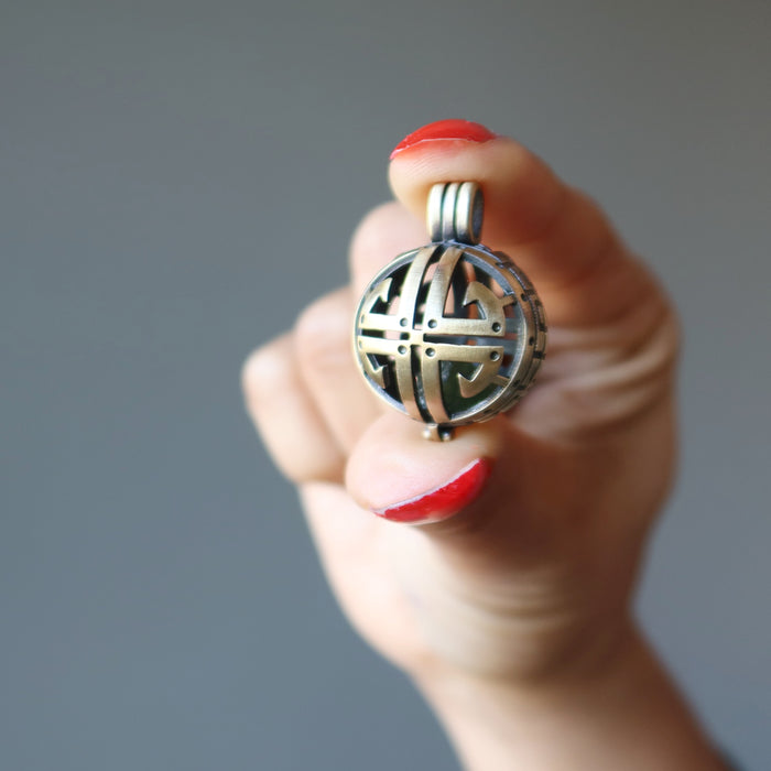 hand holding raw green moldavite in a brass cutout pendant