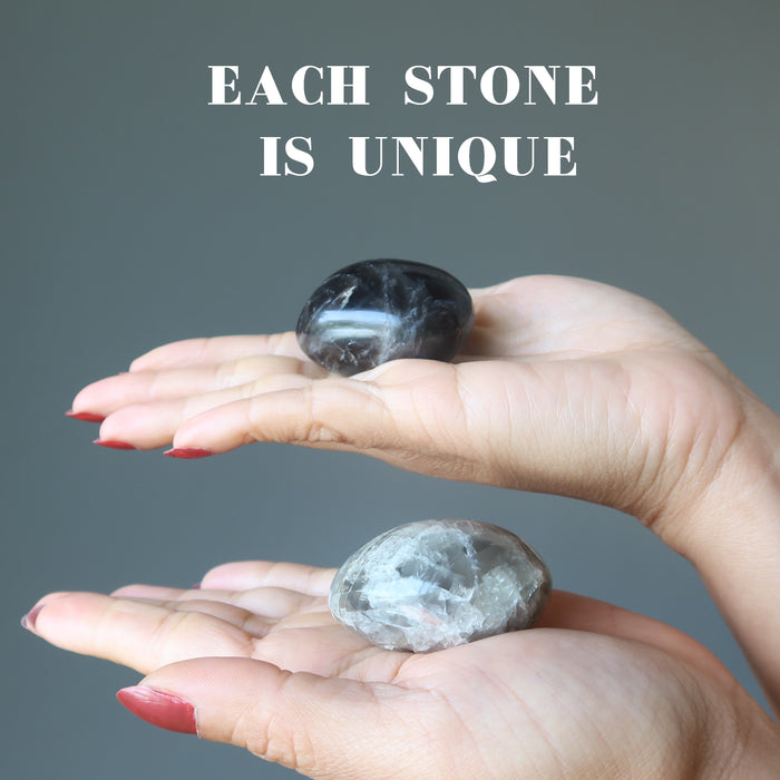 hand holding two black moonstone palm stones to show each is unique