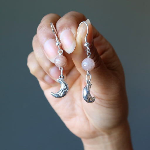 hand holding peach moonstone sterling silver crescent moon dangle earrings