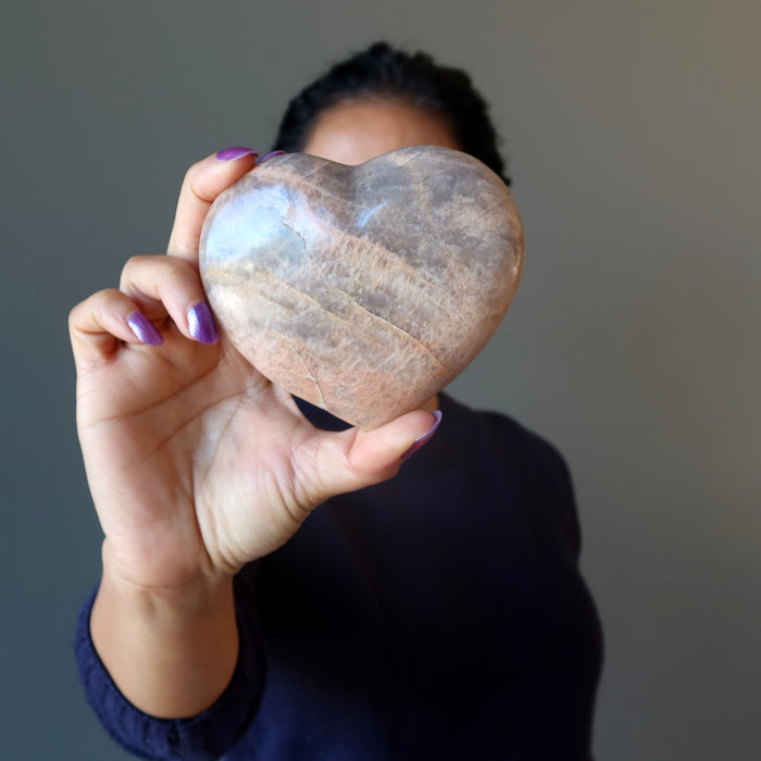 woman holding up peach moonstone heart