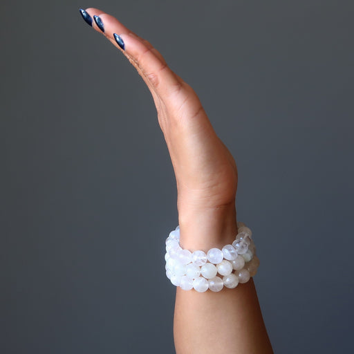 female hand wearing 3 white rainbow moonstone beaded stretch bracelets