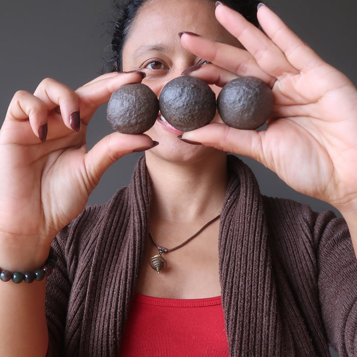 sheila of satin crystals holding three brown moqui marble stones in front of her face