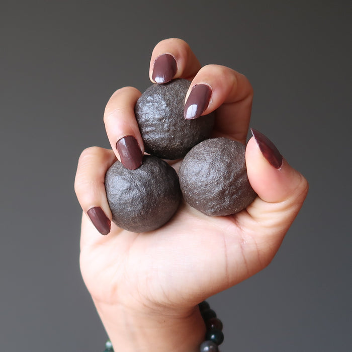 hand holding three brown moqui marble stones