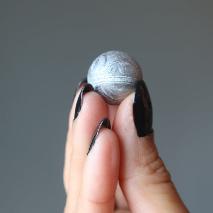 hand holding silver muonionalusta meteorite sphere