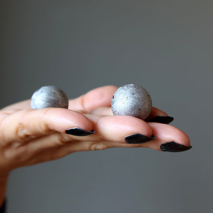 hand holding silver muonionalusta meteorite spheres