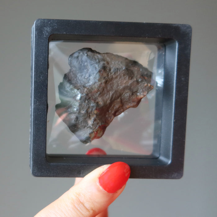 hand holding brown rocky nantan meteorite in zero gravity case