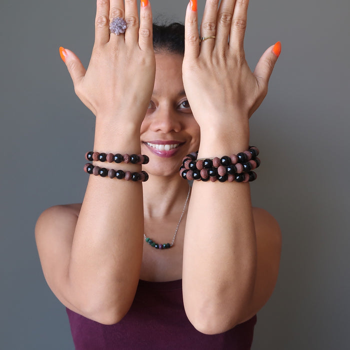 sheila of satin crystals with both hands raised wearing stacks of black obsidian and red lava bracelets