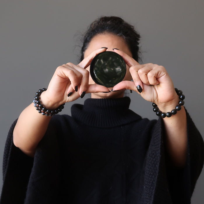 sheila of satin crystals holding an obsidian mirror in front of her face