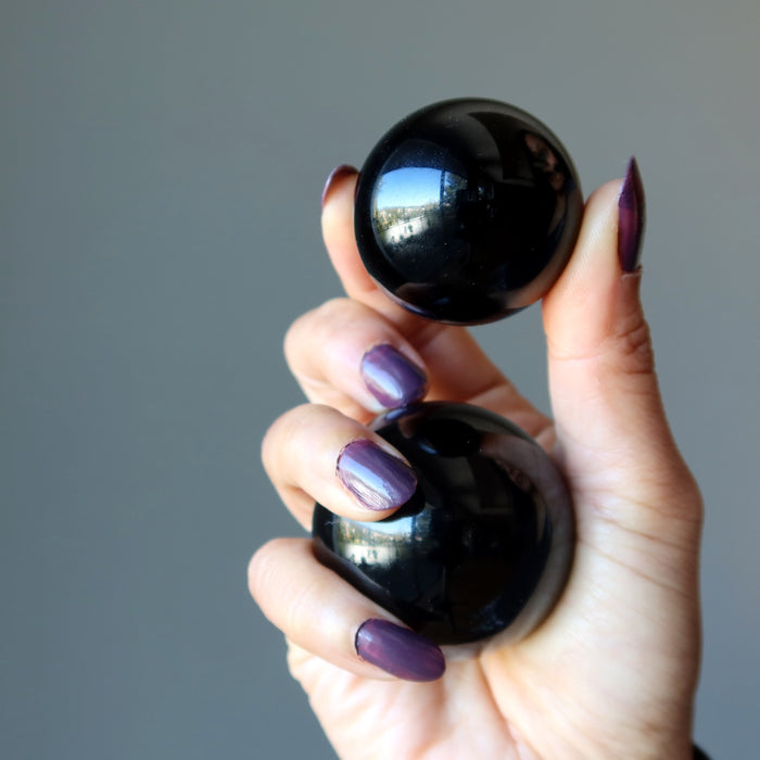 hand holding two black obsidian spheres