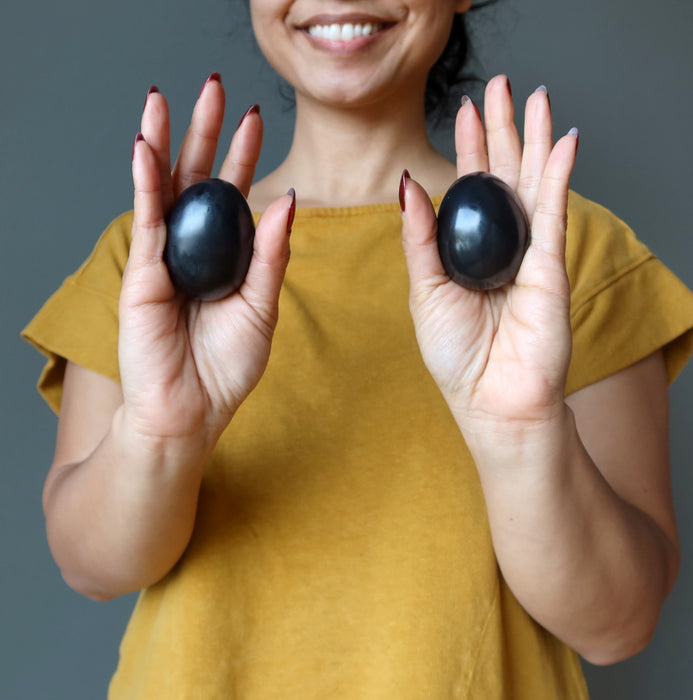 hands holding black obsidian eggs in each palm