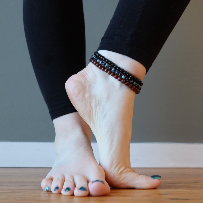 mahogany, snowflake and black obsidian anklets stacked on bare foot