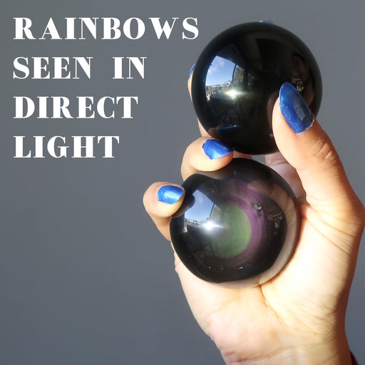 hand holding two rainbow obsidian balls, rainbows seen in direct light