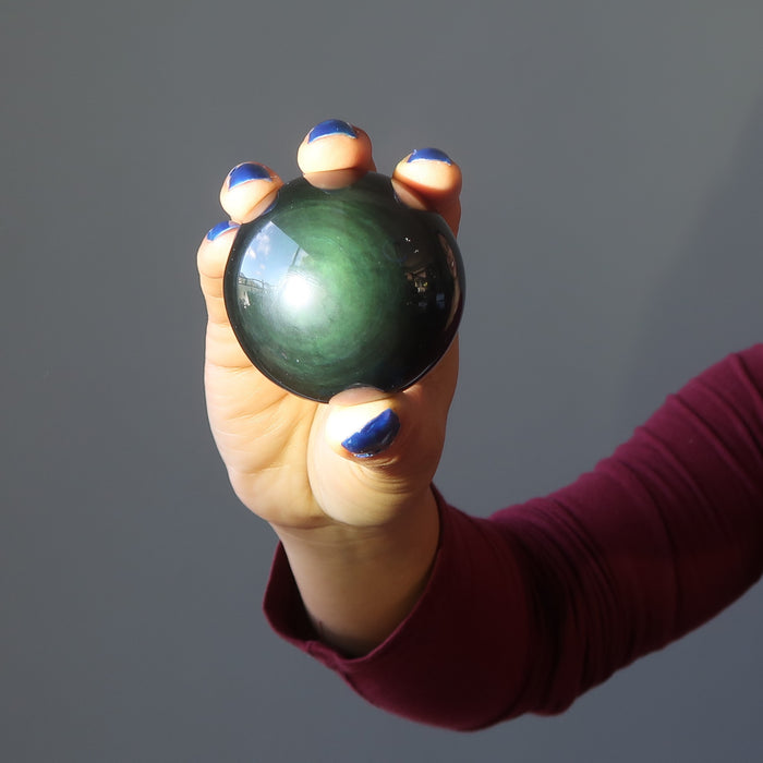 hand holding a green sheen rainbow obsidian sphere