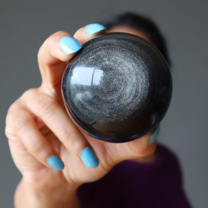 female holding silver sheen obsidian sphere in front of her face