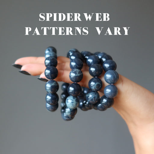 hand holding 4  round spiderweb obsidian stretch bracelets to show varying patterns
