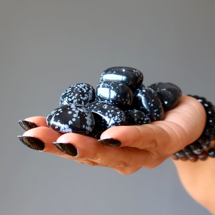 hand holding pile of snowflake obsidian tumbled stones