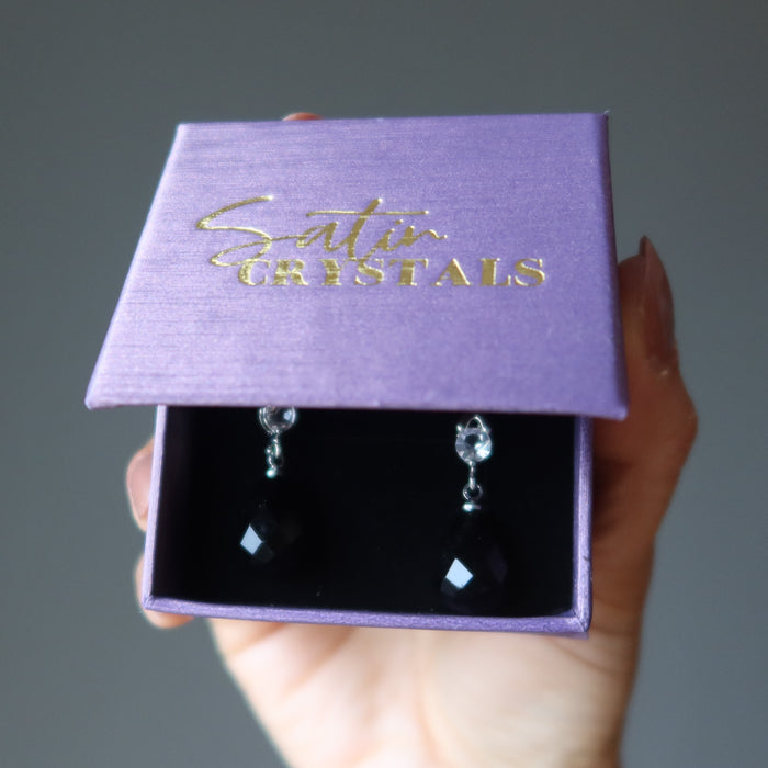 hands holding black onyx earrings in purple gift box