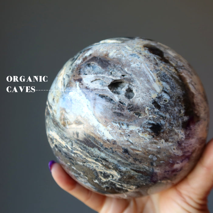 hand holding a Black Opal Sphere showing an organic caves