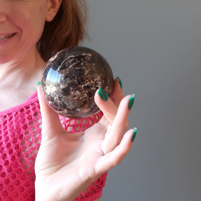 female model holding a brown opal sphere