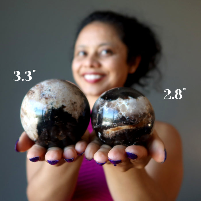 sheila of satin crystals holding two brown opal spheres showing the size difference between 2.8" and 3.3"