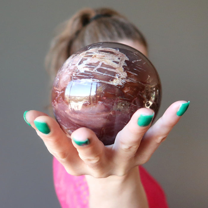 female holding petrified wood sphere in front of her face