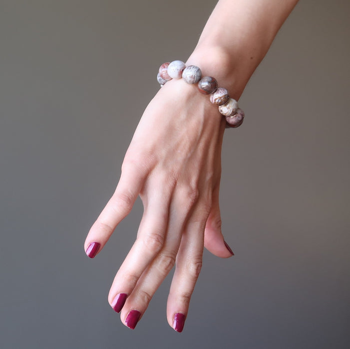 red and mosaic pietersite gemstone bracelet on the hand of a female model with matching red nail polish