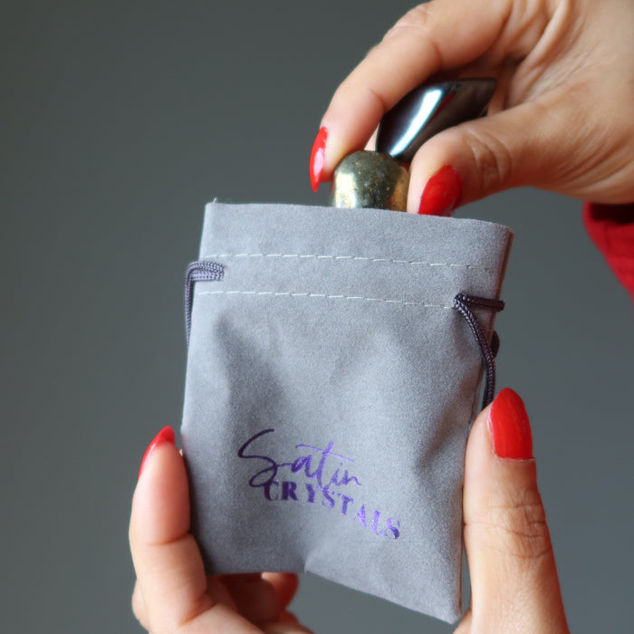 placing tumbled hematite and chalcopyrite stones in gray velvetten pouch with purple "satin crystals" print
