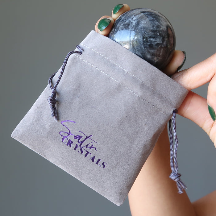 placing an aventurine sphere in a gray velvetten pouch with purple "satin crystals" print