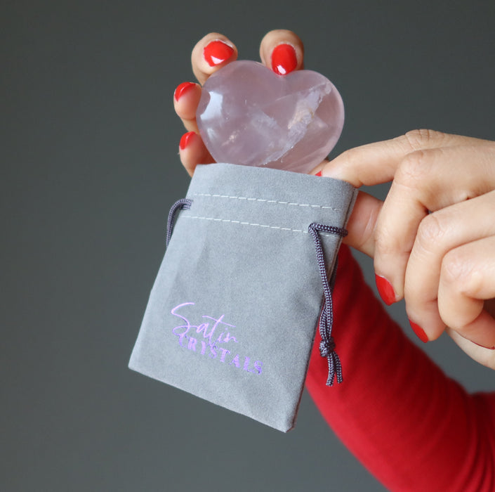 placing a rose quartz heart in a gray velvetten pouch with purple "satin crystals" print