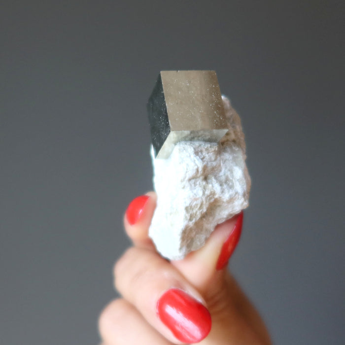 hand holding pyrite cube on white matrix to show reflective surfaces