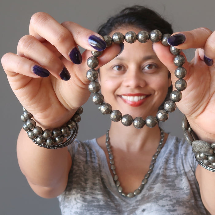 Sheila of Satin Crystals holds out a faceted golden Pyrite bracelet to display, while wearing several others on her wrists