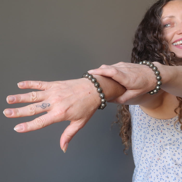 two hands outstretched and each has a golden pyrite bracelet