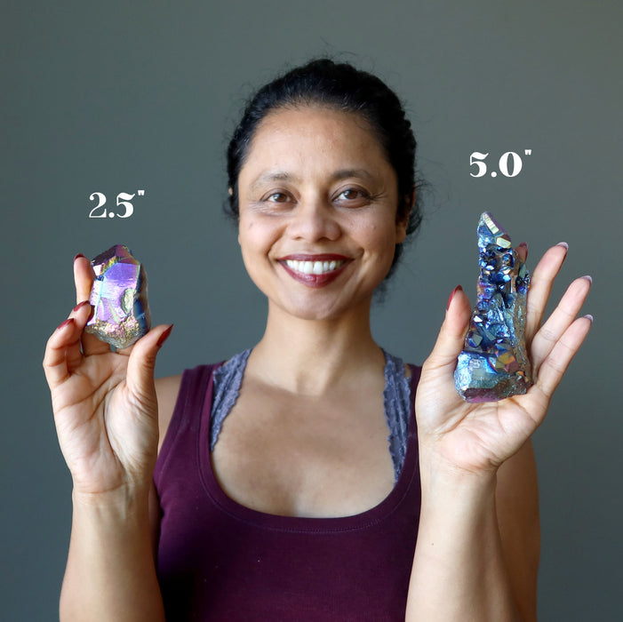 sheila of satin crystals holding two raw rainbow aura titanium quartz clusters to show size difference