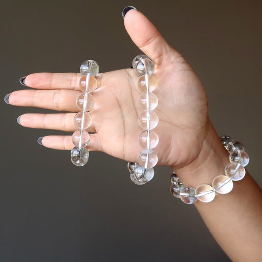 female hand wearing and holding clear quartz bracelets