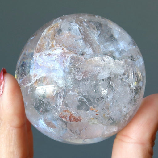 hand holding two clear quartz sphere with inclusions to show size difference