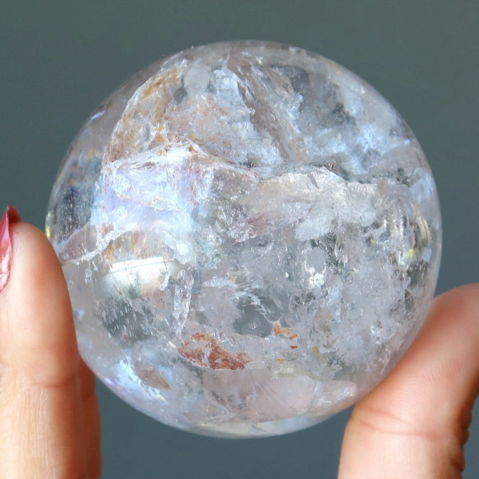 hand holding clear quartz sphere with inclusions