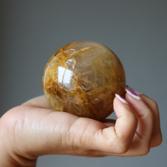 hand holding a golden quartz sphere
