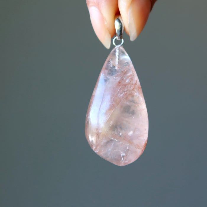 fingers holding clear quartz with red fire inclusions in teardrop pendant 