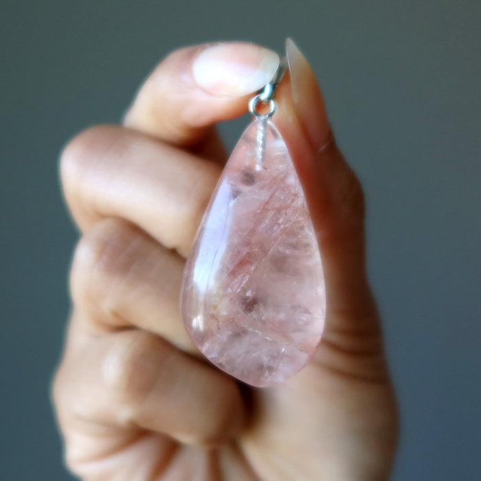 hand holding clear quartz with red fire inclusions in teardrop pendant 